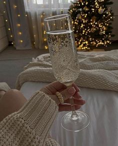 a person holding a wine glass in front of a christmas tree with lights on it