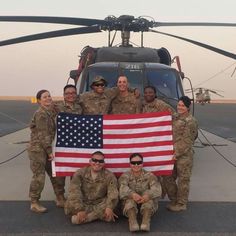 some soldiers are posing with an american flag in front of a helicopter