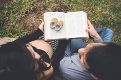 a man and woman laying on the ground reading a book with their feet propped up