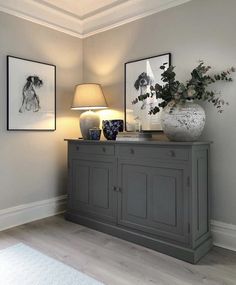 two vases on top of a gray cabinet in a room with white walls and wooden floors