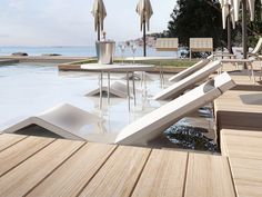 an outdoor pool with lounge chairs and umbrellas next to the water's edge