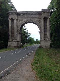 an old stone arch on the side of a road with trees in the background and grass to the side