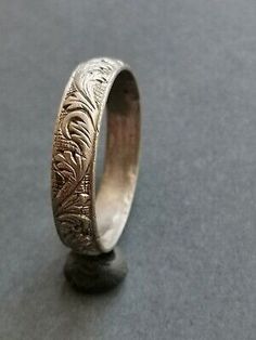 an antique silver wedding ring with engraved leaves on the inside and sides, sitting on a gray surface