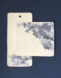 two white and blue serving trays with designs on the sides, one is holding a plate