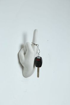 a hand holding a car key attached to a white wall with a black thumb on it