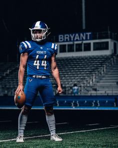 a football player in uniform holding a ball on the sidelines at night with stadium bleachers behind him