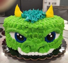 a green cake with blue and yellow frosting on it's face is decorated like a dragon