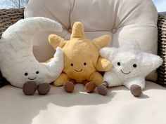 three stuffed animals are sitting on a wicker chair with white cushions and one has a yellow star