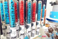 many different colored candies in glass tubes on a table with blue and red frosted cupcakes