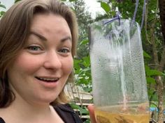 a woman is holding up a glass with liquid in it and smiling at the camera