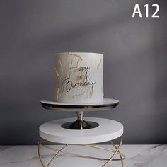 a white birthday cake sitting on top of a metal stand next to a gray wall