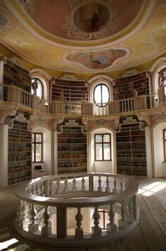 the circular room has many bookshelves and windows in it, along with a spiral staircase