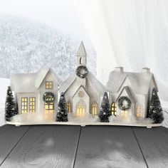 a christmas scene with a lit up house and trees in the snow on a wooden table