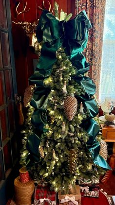 a christmas tree decorated with pine cones and green satin ribbons is shown in front of a window