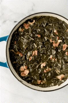 a bowl filled with collard greens on top of a white tablecloth next to a metal spoon