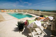 an outdoor swimming pool with lounge chairs next to it and the ocean in the background