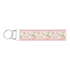 a key chain with flowers and leaves on pink fabric, hanging from a hook in front of a white background