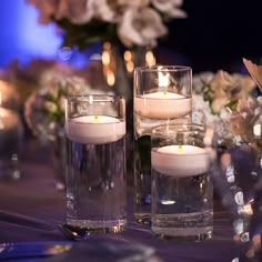 some candles are sitting on a table with flowers and glass vases in the background