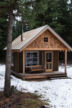 a small wooden cabin in the woods with snow on the ground and trees around it