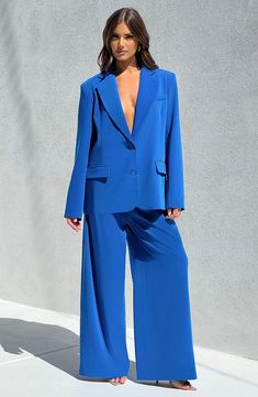 a woman in a bright blue suit and matching heels poses for the camera while standing against a wall