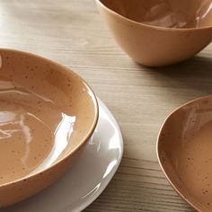 two brown bowls sitting on top of a wooden table next to white plates and utensils