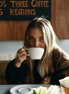 a woman sitting at a table drinking from a cup