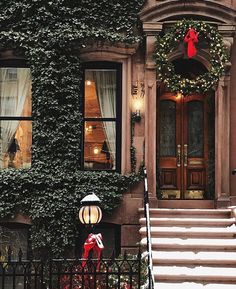 a house covered in ivy with christmas wreaths and decorations on the front door, steps leading up to it