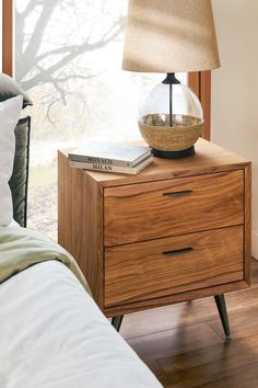 a nightstand with a lamp on top of it next to a bed and a window