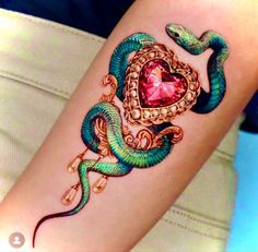 a woman's arm with a green and blue snake tattoo on it, next to a pink heart