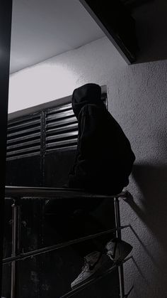 a man sitting on top of a metal chair next to a window in a dark room