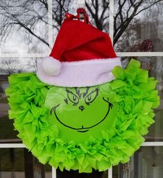 a green wreath with a grin face on it and a santa hat hanging from the front door