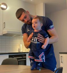 a man holding a baby in his arms while standing next to a kitchen counter top