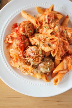 pasta with meatballs and tomato sauce in a white bowl on top of a wooden table