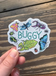 a hand holding up a sticker with bugs on it and the words buggy