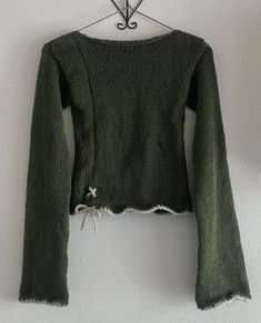 a green sweater hanging on a white wall with an iron hook and clothes pins attached to it