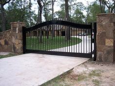 an iron gate with stone pillars in front of a driveway