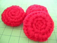 two red crocheted round objects sitting on top of a cutting board next to a ruler