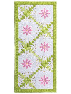 a green and white quilt with pink flowers on the front, along with an embroidered border