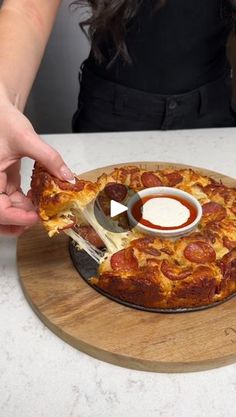 a person is holding a slice of pizza with sauce on the plate and dipping it in a small bowl