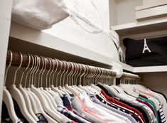 an organized closet with clothes hanging on hangers and folded t - shirts in the foreground