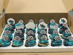 cupcakes with blue icing and white decorations in a box on a table