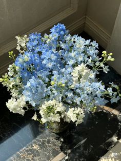 a vase filled with blue and white flowers on top of a black table next to a window