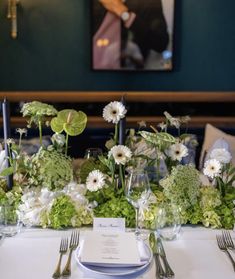 the table is set with white and green flowers, silverware, and napkins