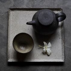 a tea pot and cup sitting on a tray with a flower in it's center