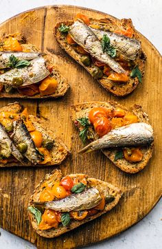 toasted bread topped with tomatoes, cheese and other toppings on a wooden cutting board