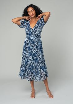 A dreamy mid-length button-front chiffon dress in an indigo blue and navy floral print. Floral print Chiffon Relaxed fit Short sleeves Mid-length Tiered skirt V-neckline Self-covered button front Adjustable back waist tie Sheer Lined Bohemian midi dress Lightweight chiffon lends an ethereal touch to this dreamy spring midi dress. Designed in a floral print, with short sleeves, a self-covered button front, and a flattering v-neckline. An adjustable tie at the back adds waist definition. Model is Blue V-neck Midi Dress With Ditsy Floral Print, Blue V-neck Floral Dress With Ditsy Print, V-neck Blue Dresses With Ditsy Floral Print, Blue V-neck Dress With Ditsy Floral Print, Blue Flowy Midi Dress With Surplice Neckline, Blue Flowy V-neck Floral Dress, Indigo V-neck Maxi Dress For Spring, Bohemian Blue Midi Dress With Ditsy Floral Print, Spring Midi Dress