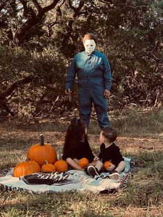 two children sitting on a blanket in front of a man with a scary mask and pumpkins