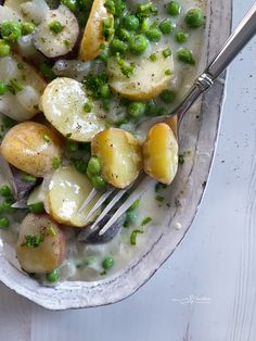 a bowl filled with potatoes and peas on top of a white table next to a fork