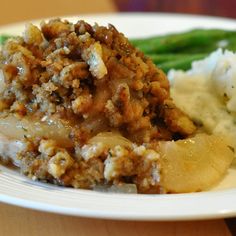 a white plate topped with mashed potatoes and meat covered in gravy next to asparagus