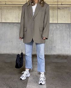 a woman standing in front of a wall holding a handbag and wearing white sneakers